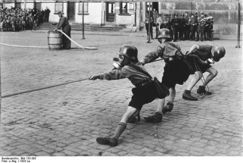 “Hitler Youth members playing tug of war while donning helmets and gas masks, 1933”